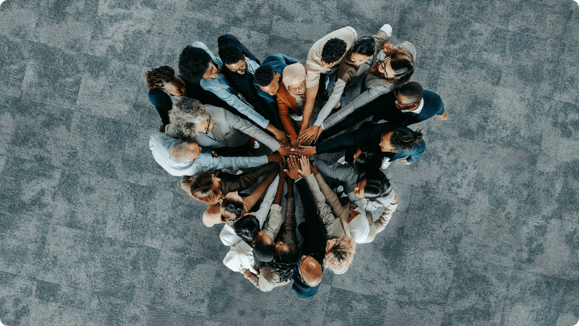Diverse group of people standing in a circle with hands stacked in center, overhead view.
